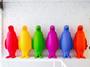 Six multicolored penguin sculptures against a white brick wall