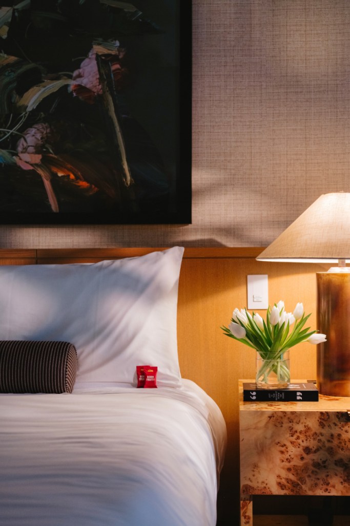 White bed with painting above it and flowers on nightstand