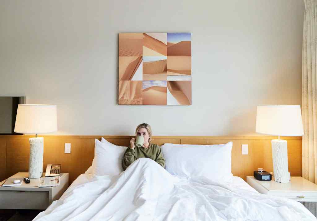 A woman in a hotel bed sipping from a mug