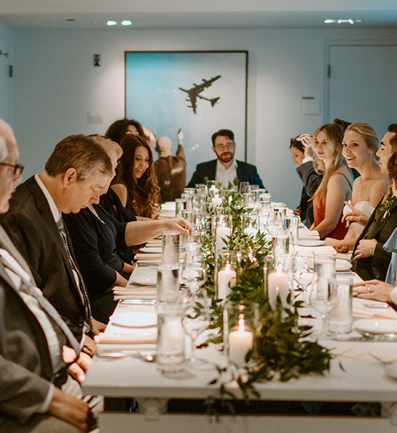 Group of dressed up people sit at a white rectangular dining table with place settings in a sleek space