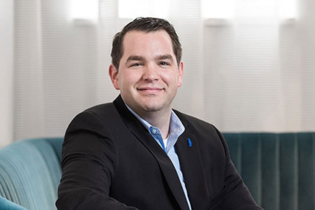 Man in suit coat smiles at the camera