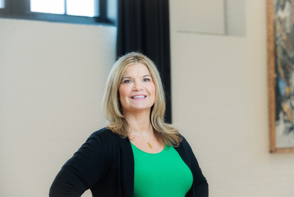 Woman in green shirt and black sweater smiles at the camera