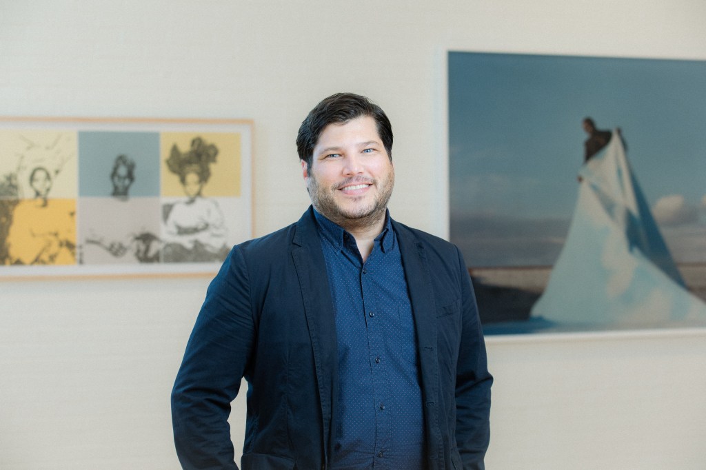 Man in blue shirt and blazer smiles at the camera