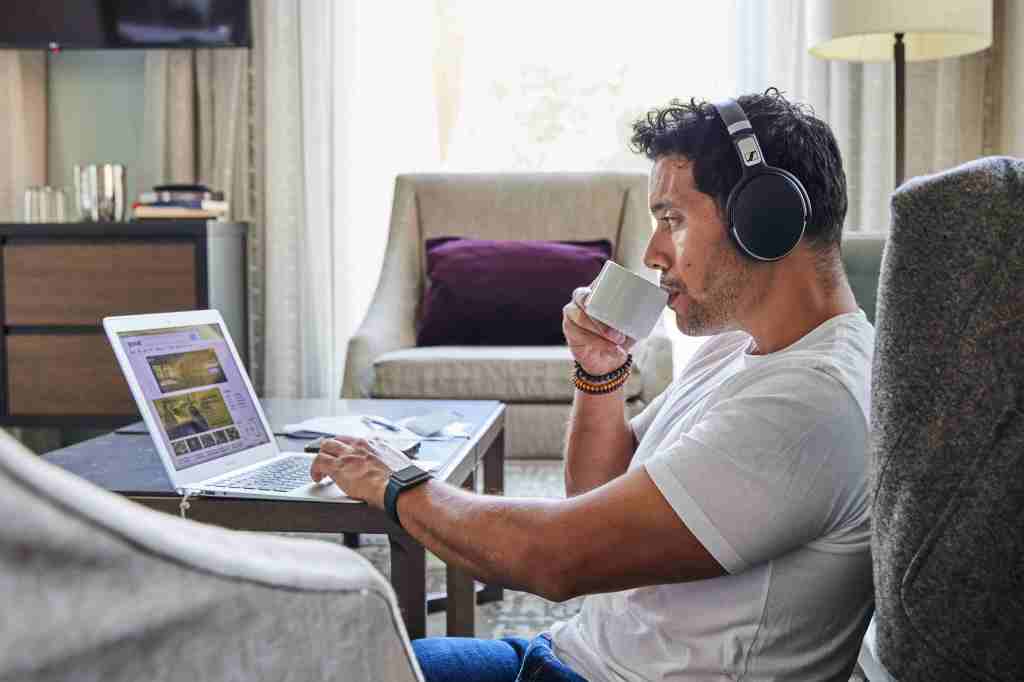 A man sipping a mug of coffee while working on a laptop from a 21c Louisville hotel room
