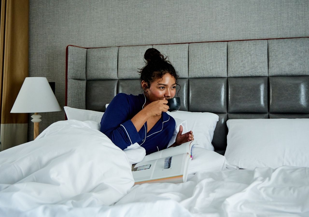 A woman sipping from a mug in a king hotel bed at 21c St. Louis
