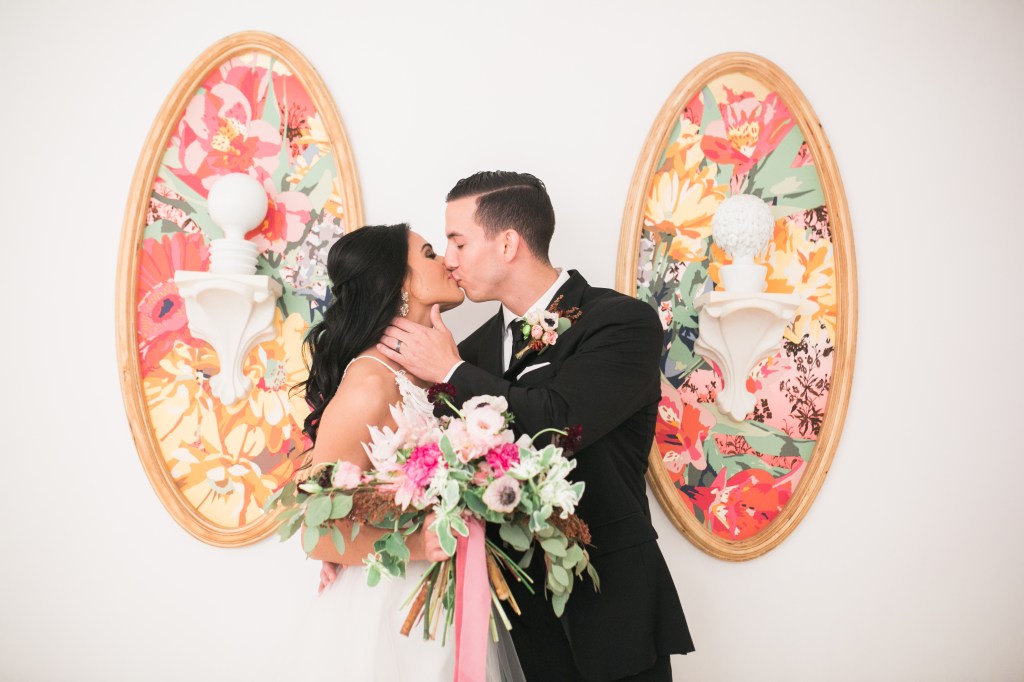 Newlyweds embracing in front of colorful artwork