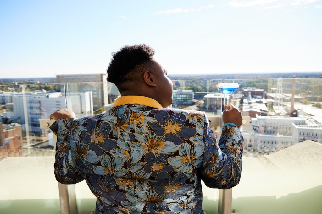 Man in colorful suit jacket looks out from a rooftop