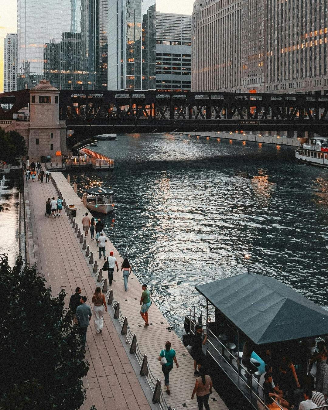 River with a concrete sidewalk with people walking on it and a bridge in the background