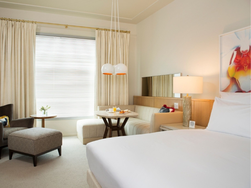 Large white bed in hotel suite with sofa, lounge chair, and table