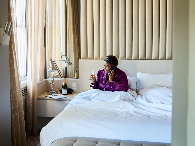 Woman on phone laying in bed with champagne glass in hand