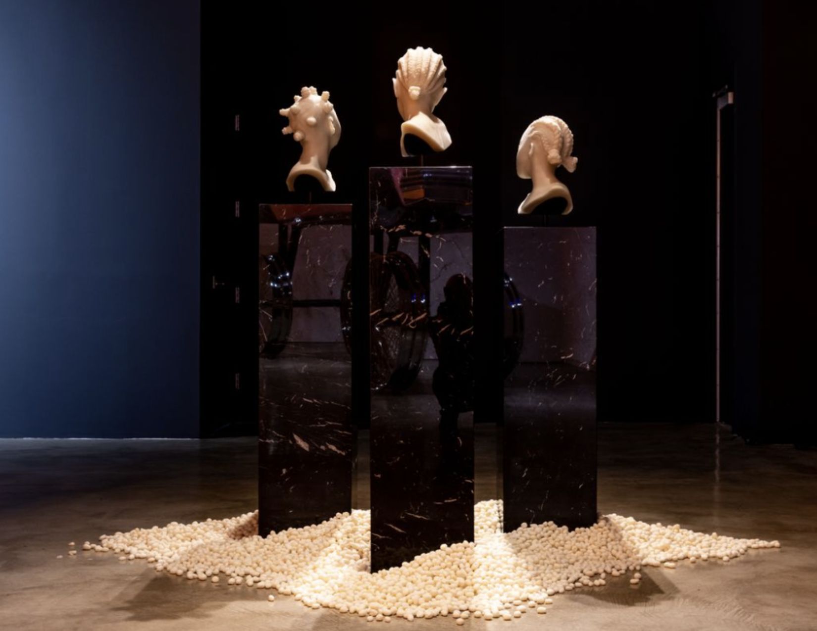 Three shea butter busts of young Black girls in protective hairstyles sitting atop black Italian marble engulfed in hand-carved shea nuts.