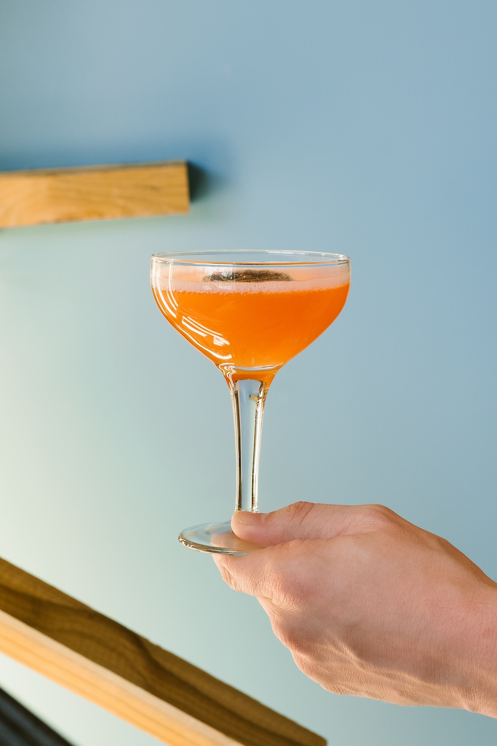 Orange cocktail in a coupe glass being held up with a hand