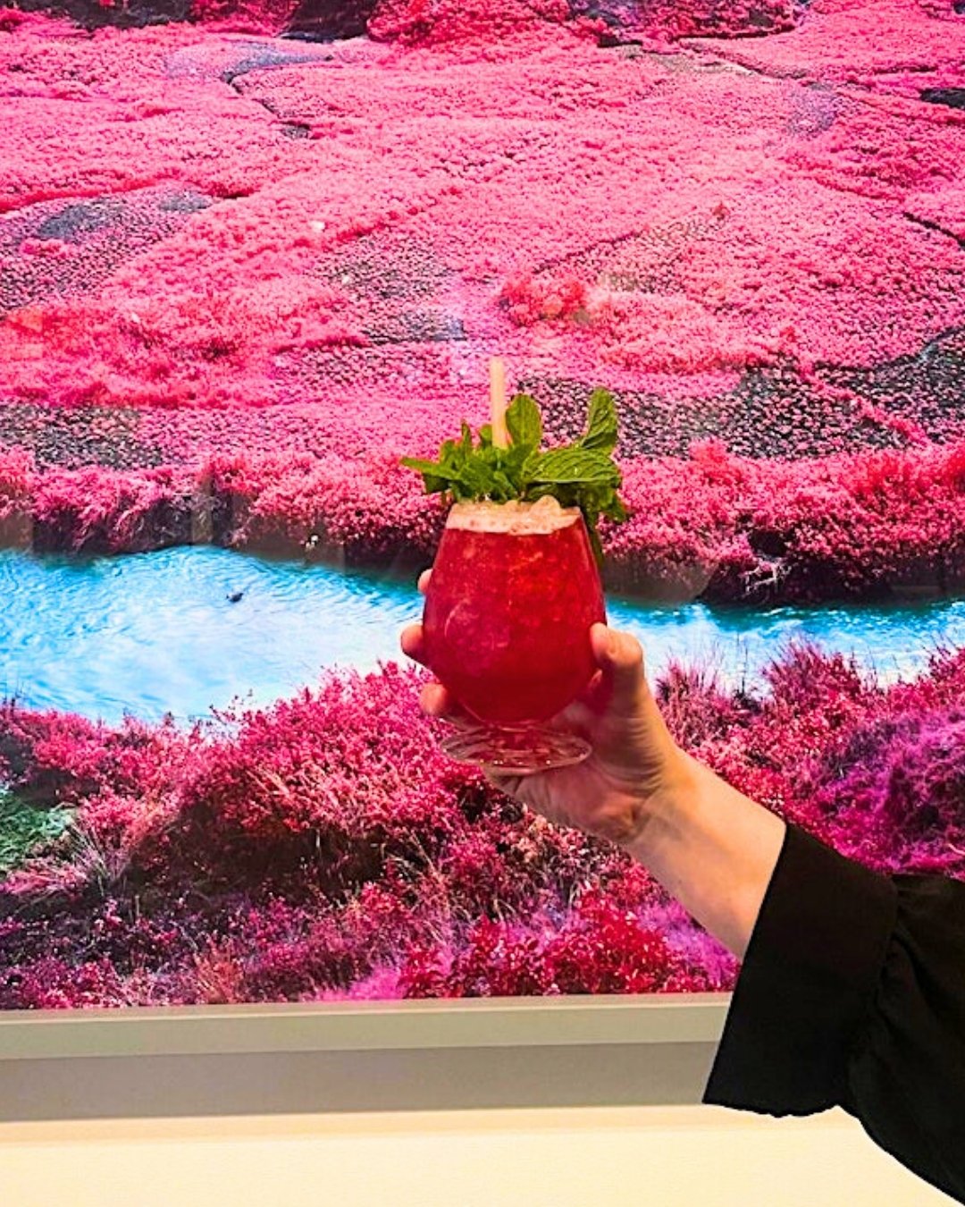 Pink cocktail being held in front of art work
