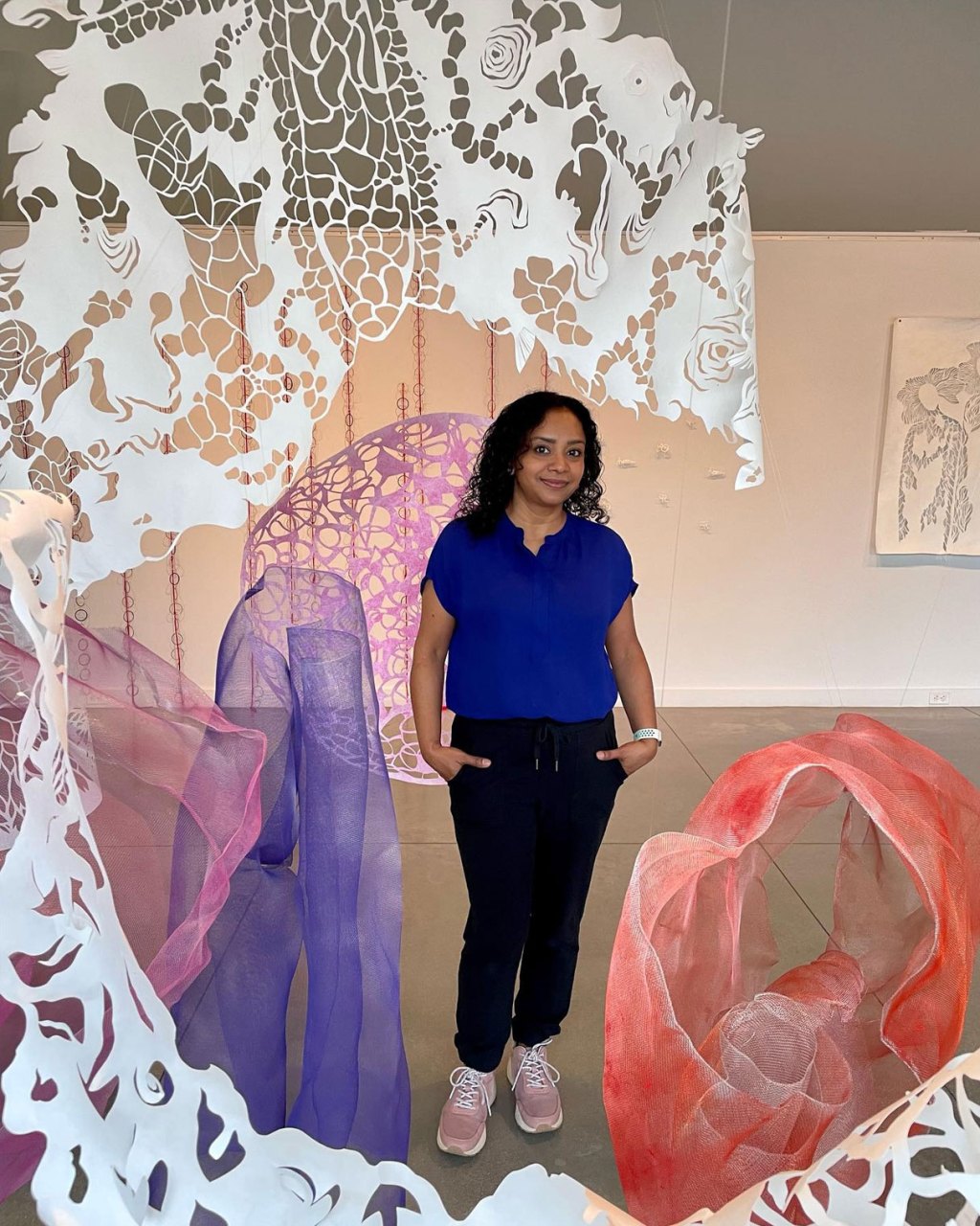 Artist Sukanya Mani standing behind her paper cut-out art installation